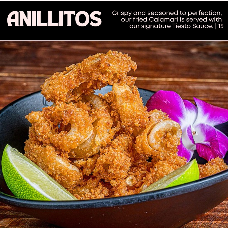 Crispy fried calamari rings with lime wedges and a purple orchid in a black bowl.