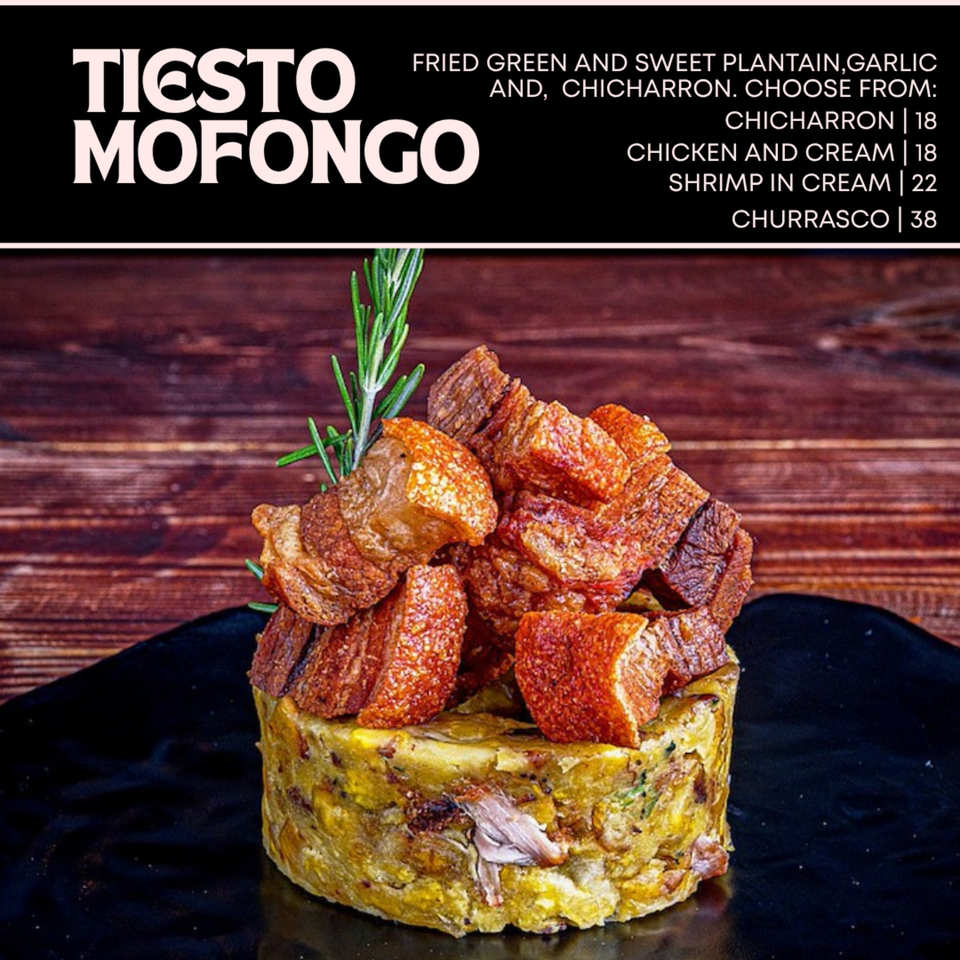 Tiesto Mofongo with crispy chicharron and a rosemary sprig on a dark plate.